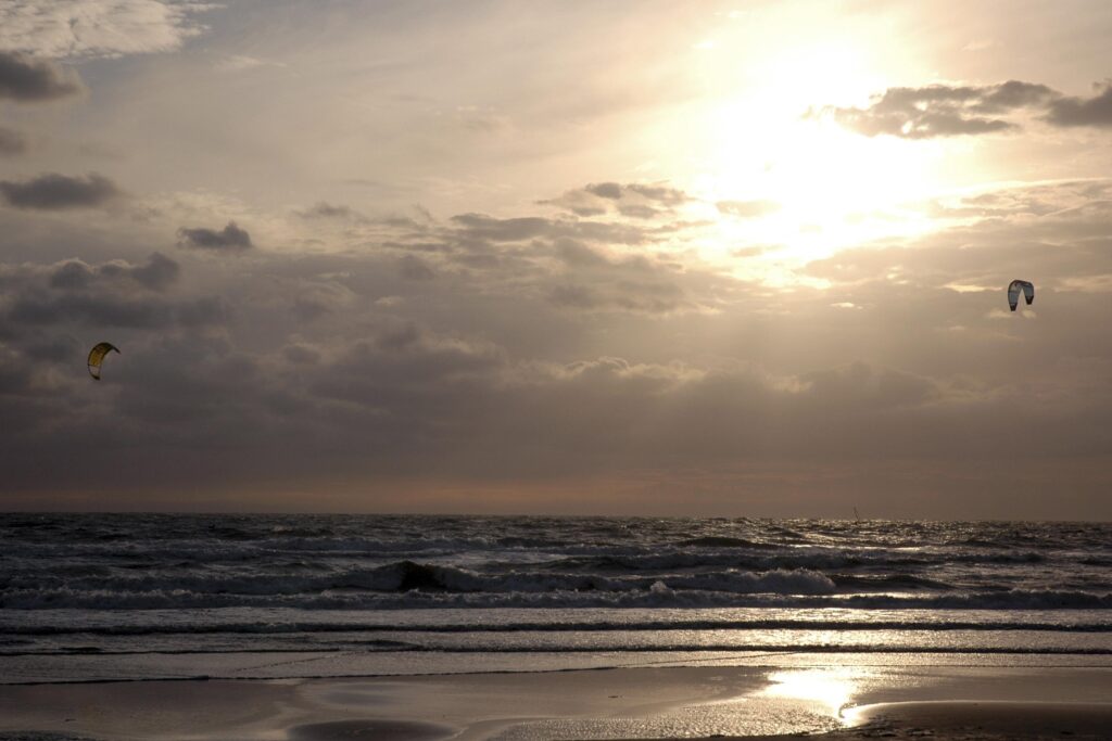 Zonsondergang over de zee met kite surfers die door de golven glijden.