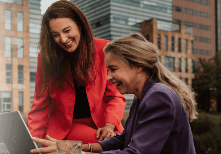 Twee collega's zitten buiten te overleggen achter een laopt.