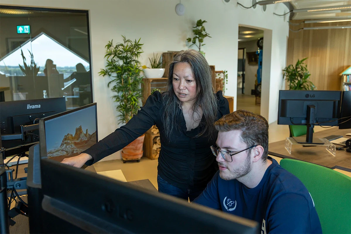 Twee collega's zijn kantoor en overleggen samen achter een computer.