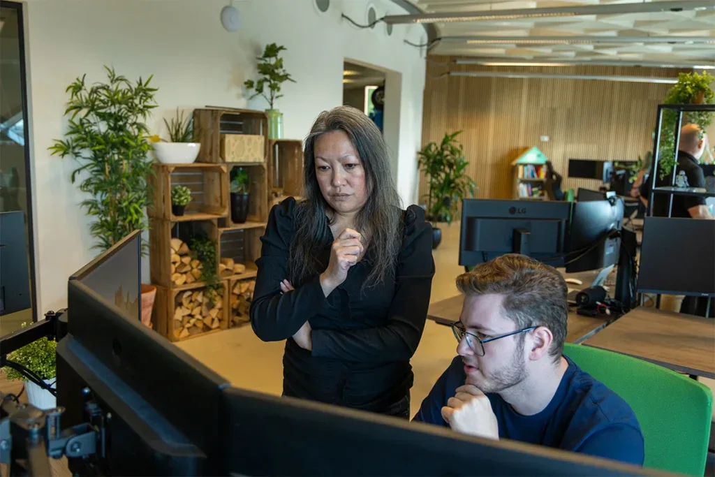 Twee collega's zijn kantoor en overleggen samen achter een computer.