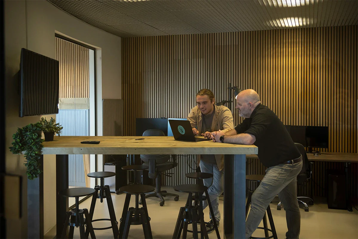 Twee collega's kijken naar een laptop en overleggen in de vergaderkamer.