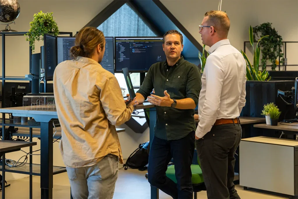 Drie developers staan bij een bureau en overleggen op kantoor.