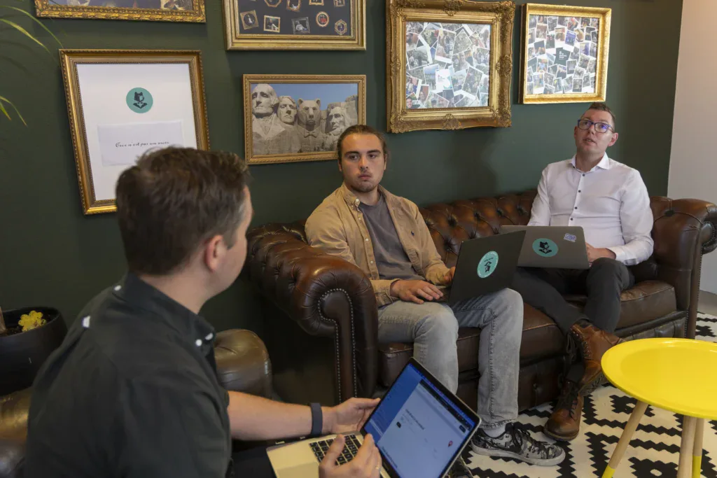 Developers overleggen met hun laptop op schoot op een leren bank.