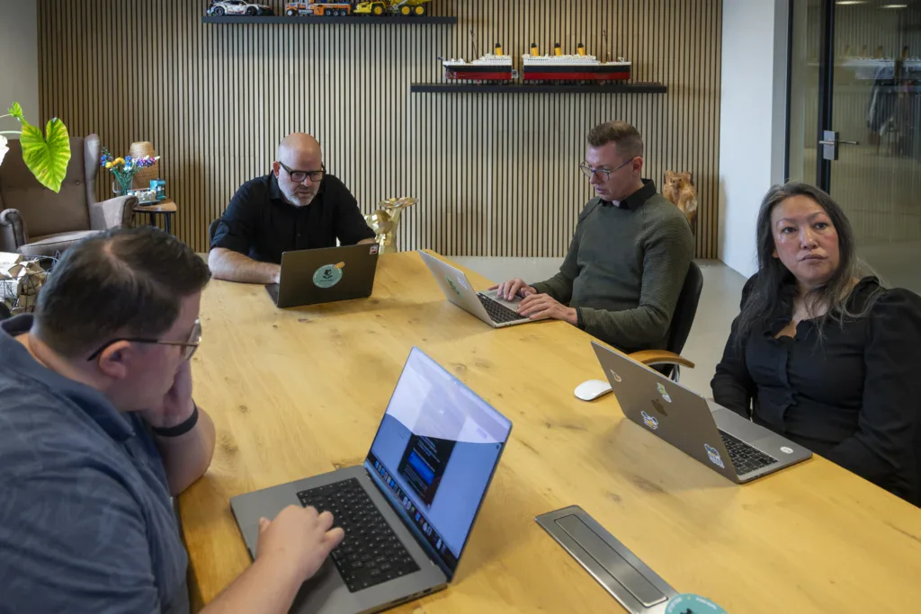 Directie zit aan een tafel in de vergaderkamer en kijkt naar een scherm.