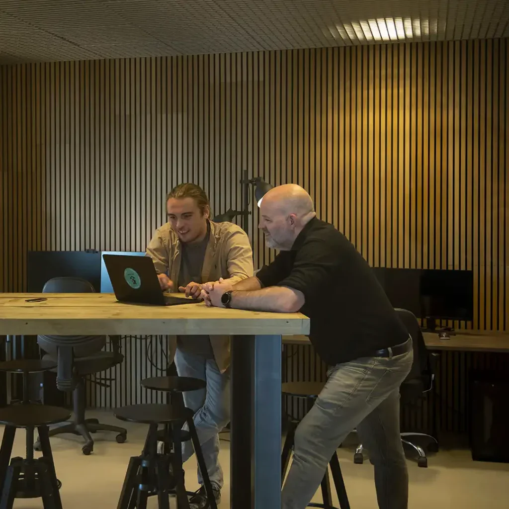 Collega's overleggen in de teamkamer en kijken naar een laptopscherm.