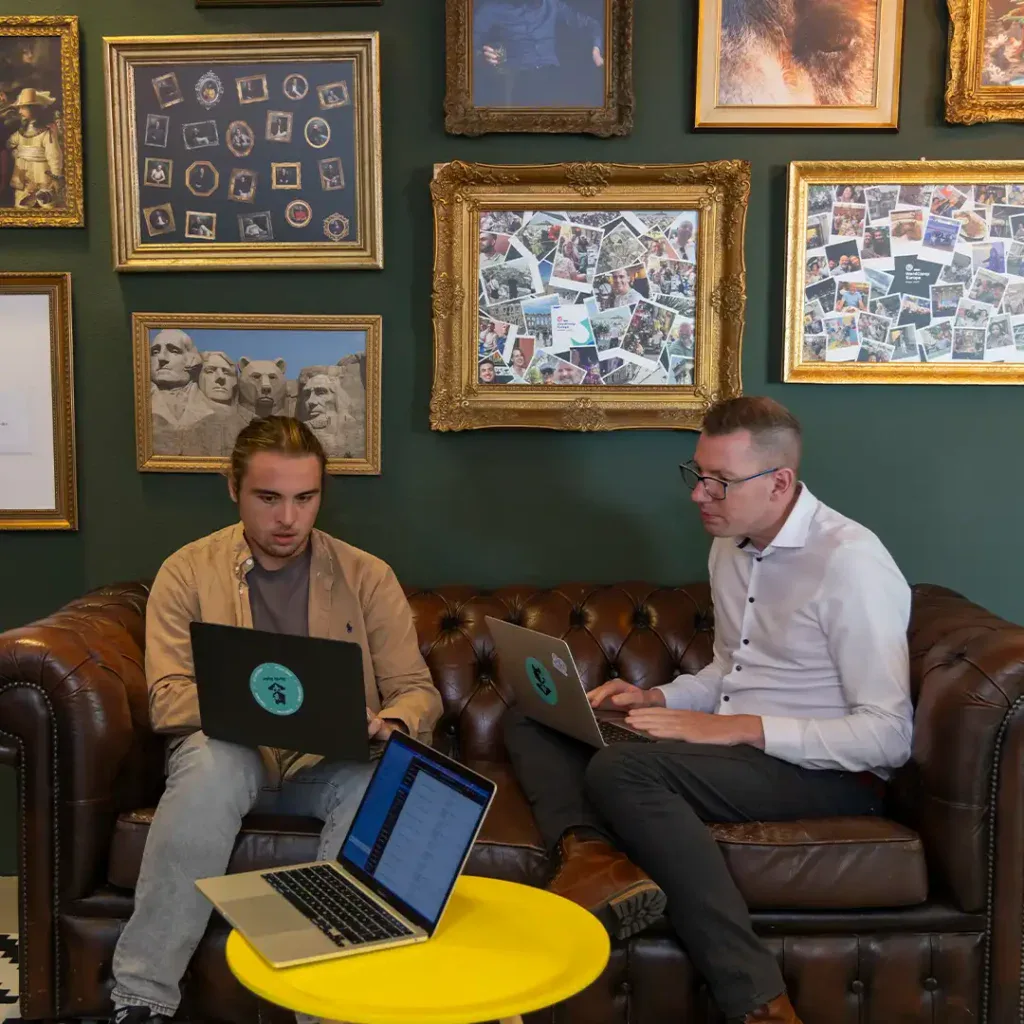 Developers zitten samen op een leren bank en kijken naar een laptopscherm.